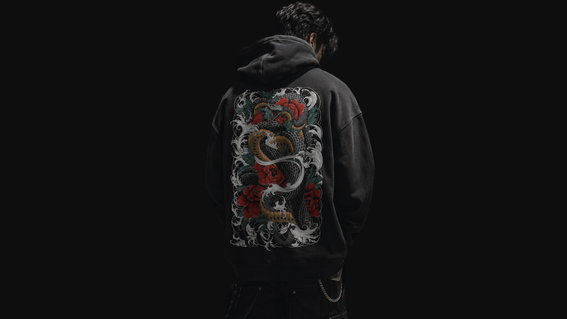 Man wearing a black hoodie with a large Irezumi inspired snake, wave and red flower back print in a dark streetwear style.