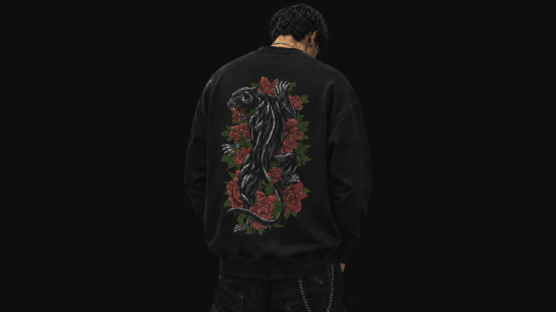 Person wearing a black sweatshirt with a panther and floral design on the back against a black background